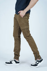 A male model wearing olive brown cargo pants with a blue polo shirt, standing on one leg to show the fit and style of the pants. -  Men's Cargo Pant - Olive Brown - Xea Clothing